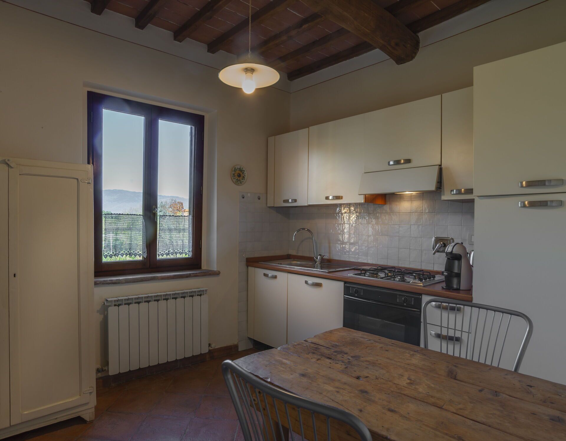 A kitchen with white cabinets, a wooden table, a window with a view, and a radiator.