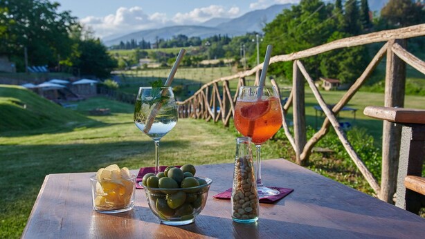 Una mesa de picnic con bebidas, aceitunas y un frasco de nueces.