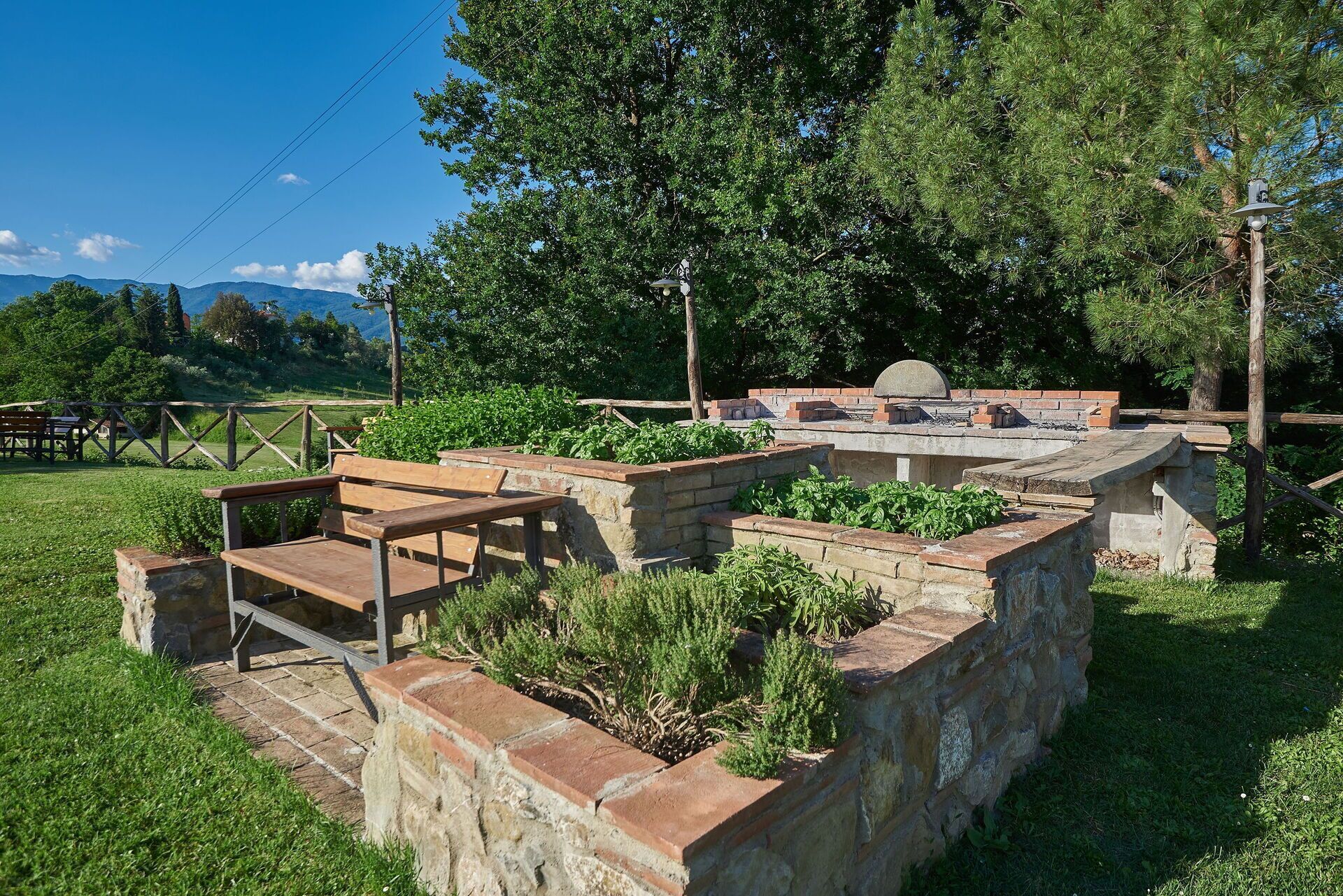 A stone patio with a wooden bench, surrounded by greenery and a stone wall.