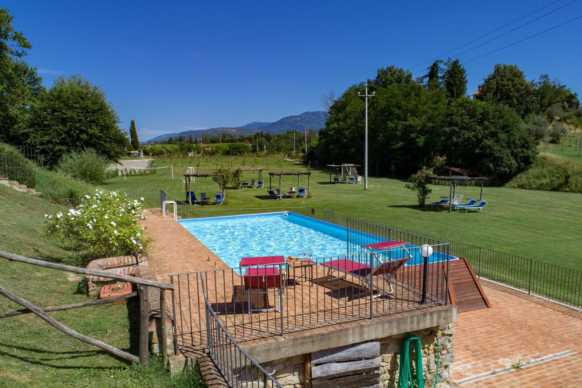 Una piscina con solárium, rodeada por un área verde con sillones de descanso y una pérgola.