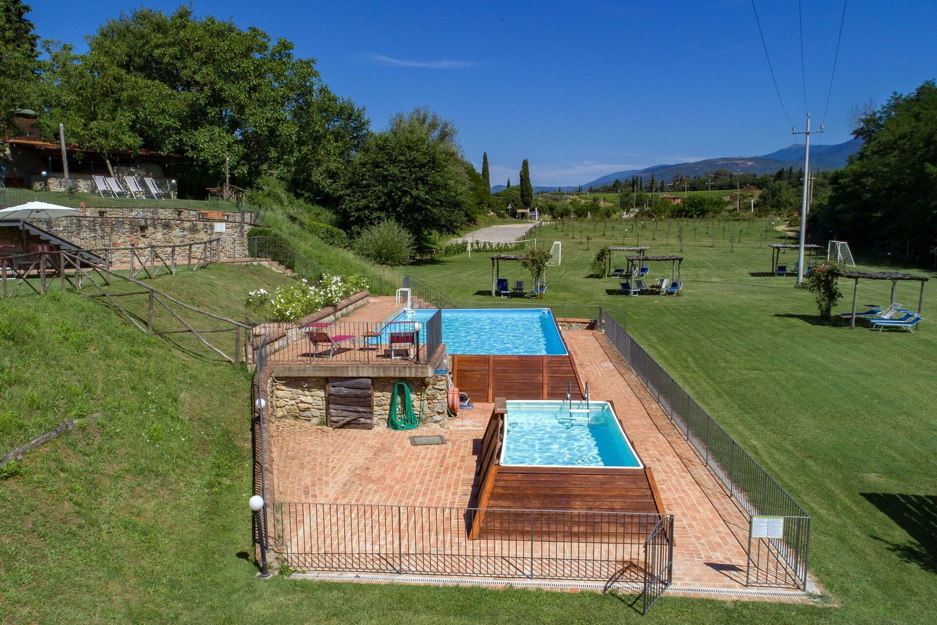 A backyard with a swimming pool, a stone wall, and a grassy area with trees.