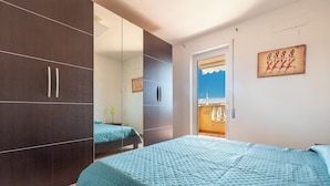 A bedroom with a large wardrobe, a bed with a blue quilt, and a painting on the wall. - 3895 RSM - Appartamento Ester by Barbarhouse (Manduria)