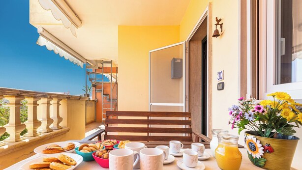 A balcony with a table set for breakfast, including pastries, mugs, and a flower vase. - 3895 RSM - Appartamento Ester by Barbarhouse (Manduria)