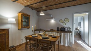 A rustic kitchen with a wooden table set for dining, a cabinet, and a hanging light fixture. - Le Fornaci - Apartment with pool (Latereto)
