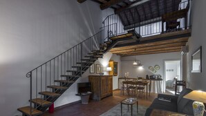 A spacious living area with a wooden staircase, a dining table, and a sofa. - Le Fornaci - Apartment with pool (Latereto)