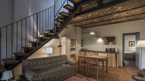 A cozy living room with a patterned sofa, a dining table, and a kitchen area with a microwave. - Le Fornaci - Apartment with pool (Latereto)
