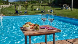 A poolside table with a meal and two glasses of white wine, surrounded by a clear blue pool and a scenic view of mountains and greenery. - Le Fornaci - Apartment with pool (Latereto)