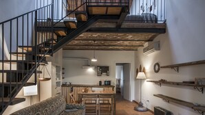 A spacious living area with a staircase, a sofa, a dining table, and a kitchen in the background. - Le Fornaci - Apartment with pool (Latereto)