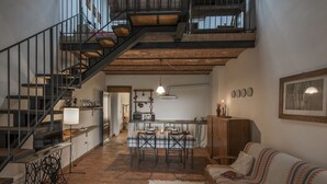 Un loft espacioso con techo alto, paredes de ladrillo visto, una escalera, una zona de comedor con mesa y sillas, un sofá y una cocina.