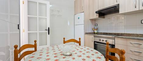 A kitchen with wooden cabinets, a refrigerator, an oven, and a dining table with chairs.