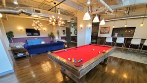 A pool table in a room with wooden flooring, a blue sofa, and pendant lighting.