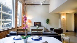 A dining area with a round table, chairs, and a bench. There is a potted plant and a painting on the wall.