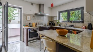 A modern kitchen with a large island, stainless steel appliances, and a view of greenery outside. - Casa das Fontes – House of Wells with Mountain View, Private Garden and Wi-Fi (Parede)