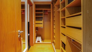 A walk-in closet with wooden shelving, a step stool, and hanging garments. - Casa das Fontes – House of Wells with Mountain View, Private Garden and Wi-Fi (Parede)
