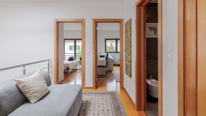 A modern room with a grey sofa, a patterned rug, and a wooden door leading to a bathroom. - Casa das Fontes – House of Wells with Mountain View, Private Garden and Wi-Fi (Parede)