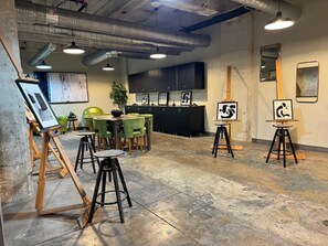 An art gallery with paintings on easels, a reception desk, and a seating area with chairs and tables.
