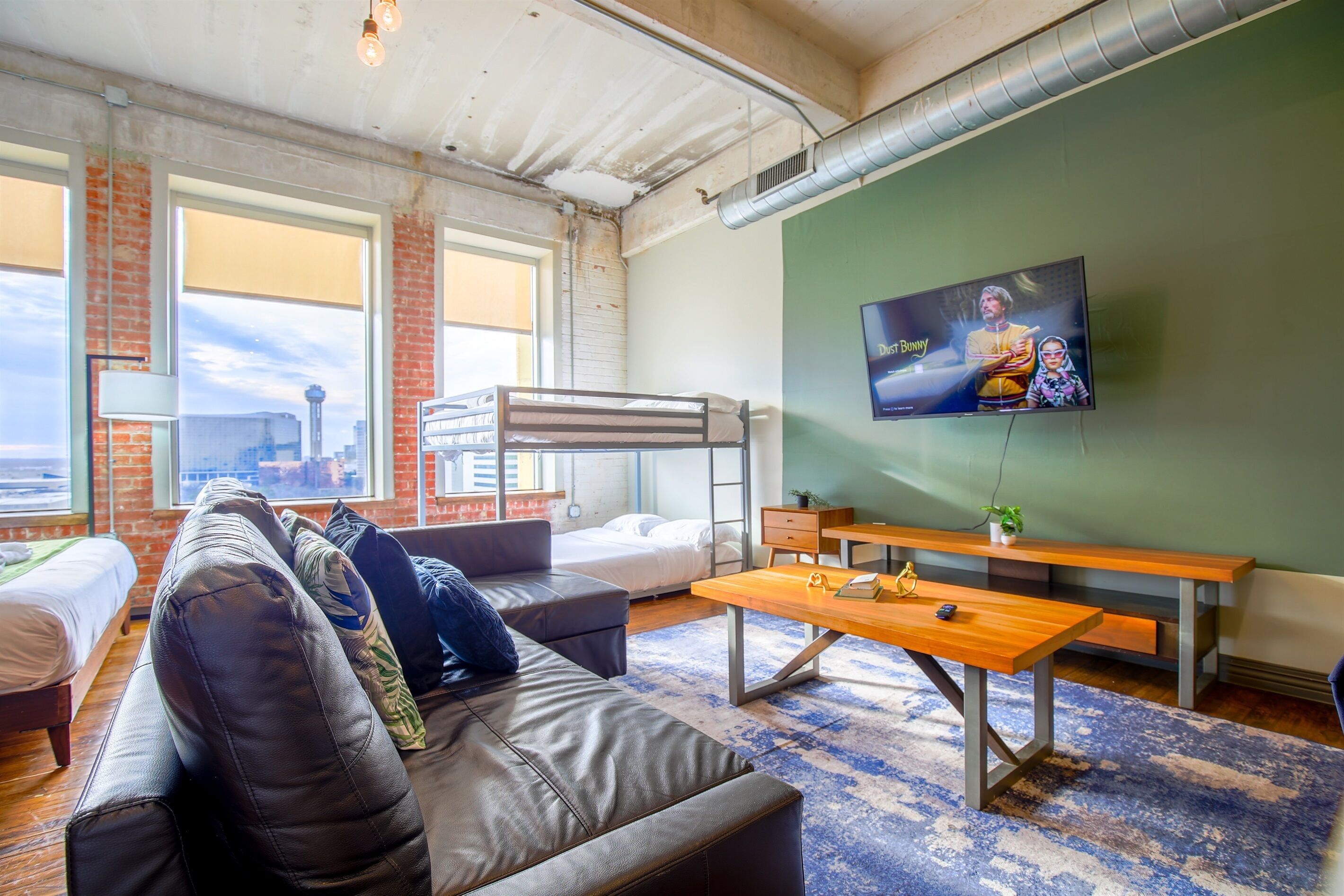 A modern, well-lit room with a bunk bed, a sofa, a wooden table, and a TV mounted on the wall.