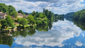 Une rivière paisible qui reflète le ciel et la végétation environnante, avec des bâtiments situés sur la rive gauche.