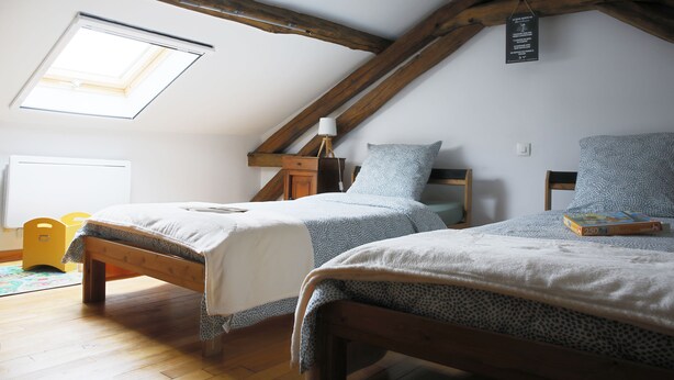 Une chambre avec deux lits, une lucarne, des poutres apparentes et une table de chevet avec une lampe.