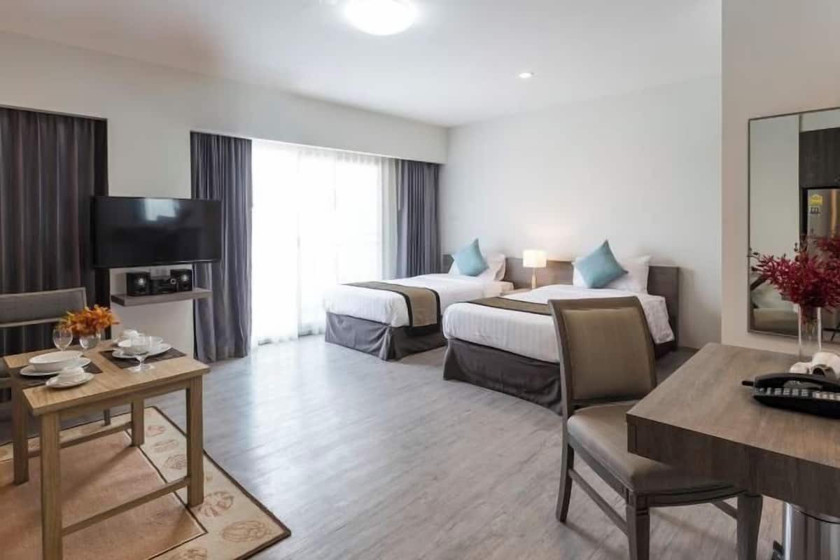 A hotel room with two beds, a TV, a dining table, and a large window.