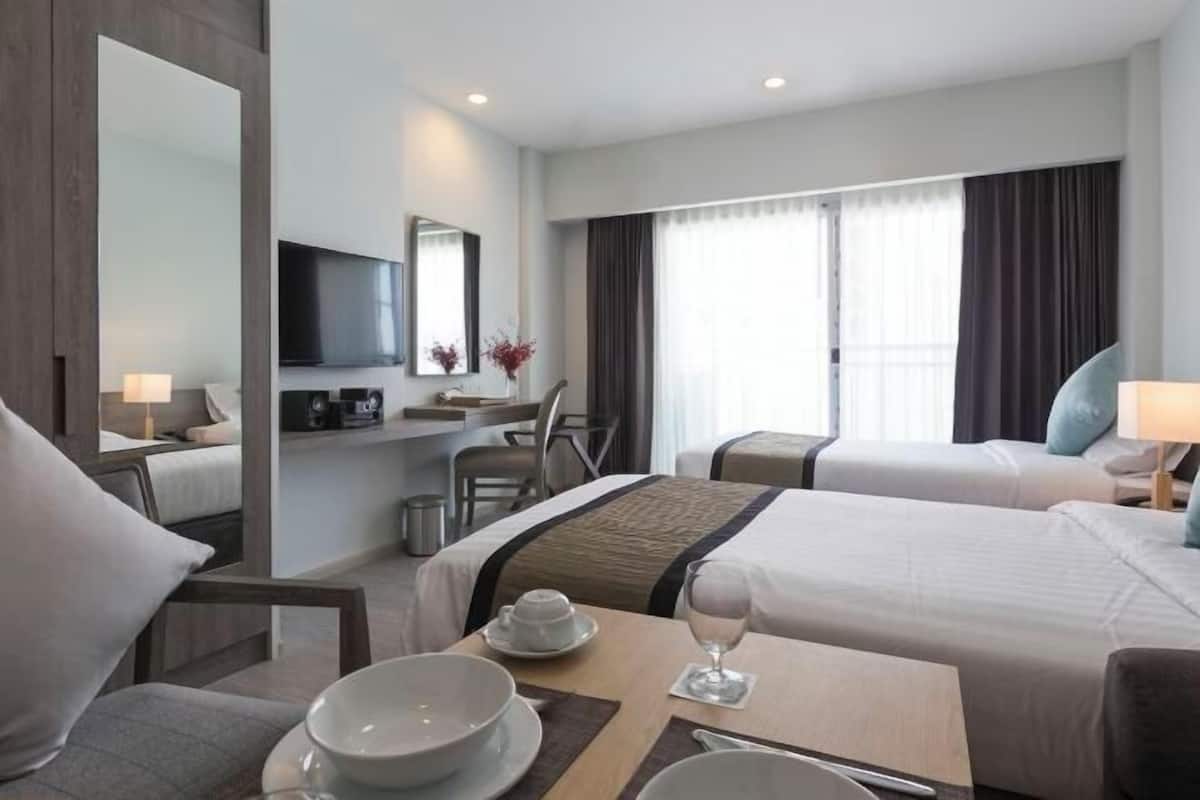 A hotel room with two beds, a desk, a TV, and a window with curtains.