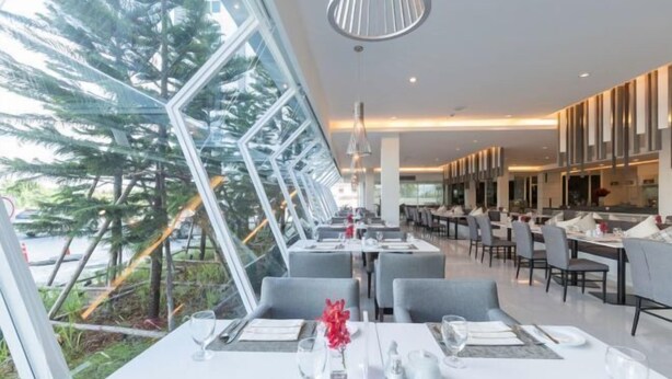 En moderne restaurant med et aflangt spiseområde, store vinduer og udsigt til træer.