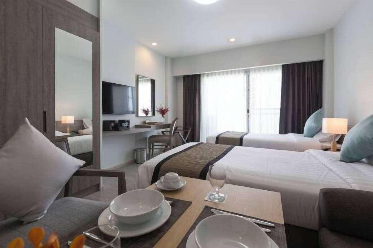 A hotel room with a bed, a desk, a TV, and a dining area with a table set for two.