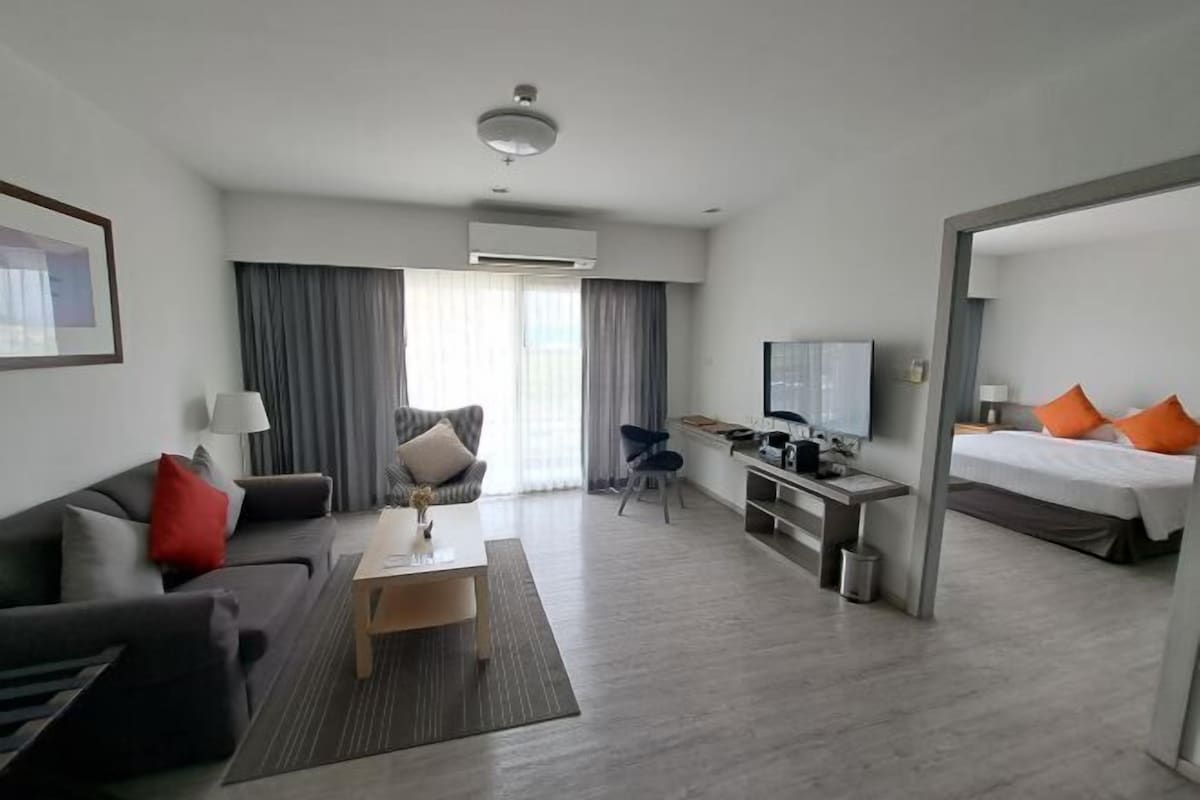 Una habitación de hotel moderna con sofá, mesa de centro, televisor, escritorio y cama.