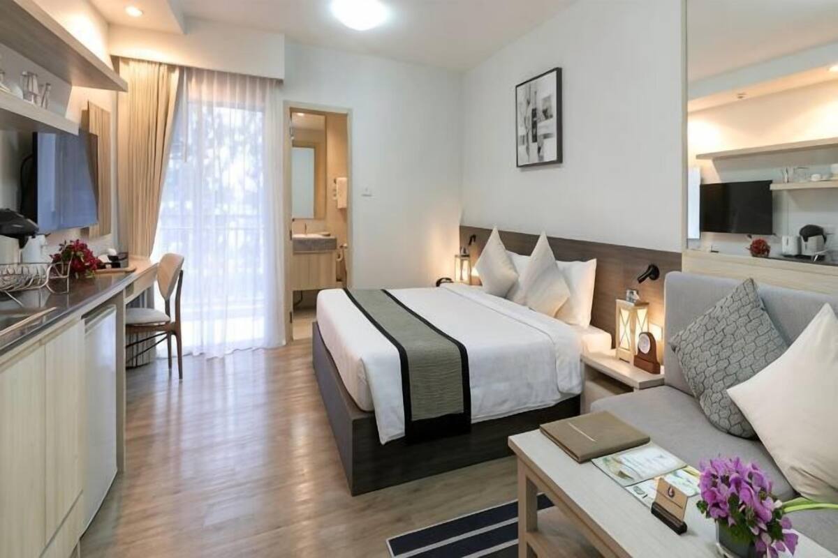 A hotel room with a bed, a desk, a chair, a sofa, a TV, and a bathroom.
