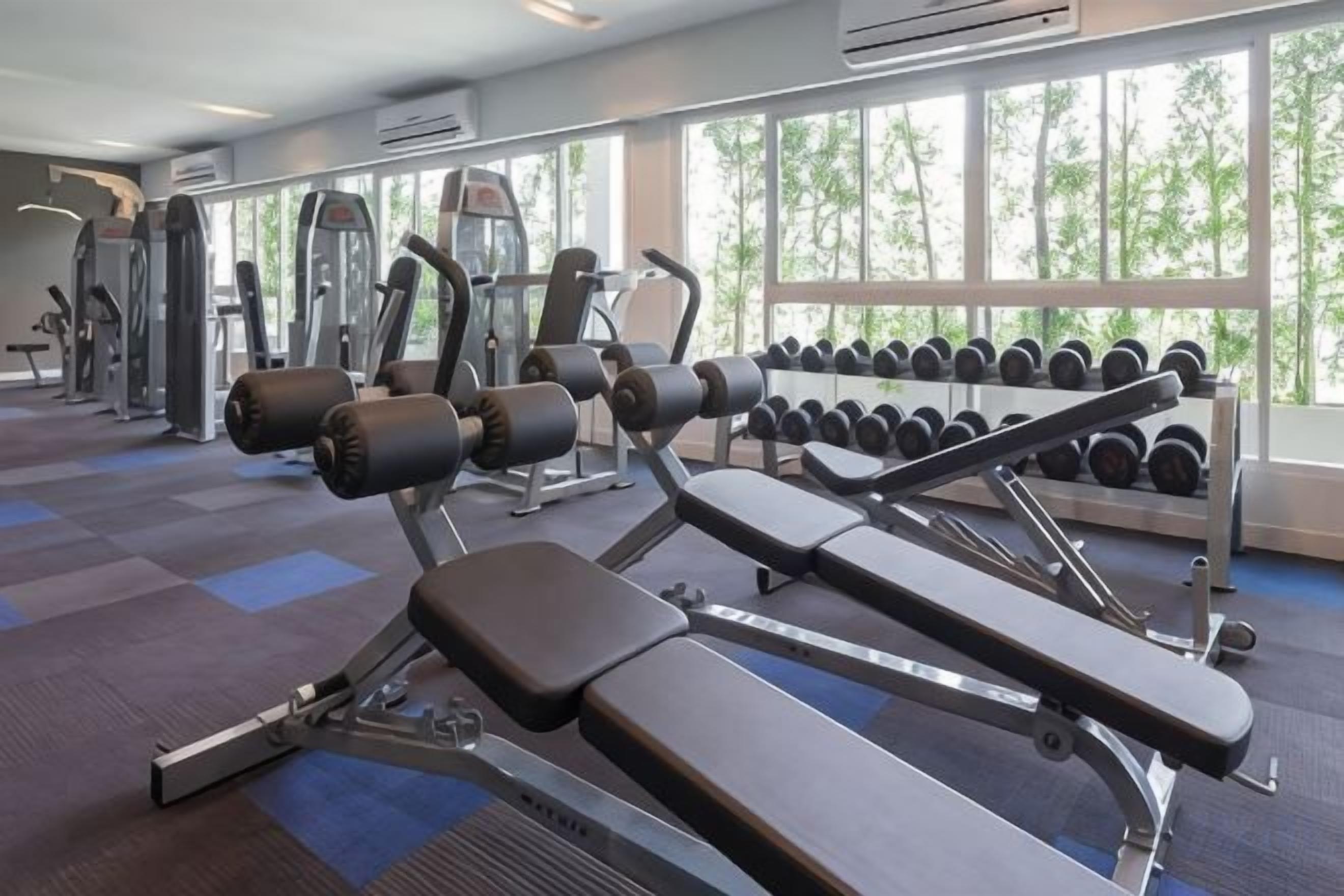 Une salle de sport équipée de machines d’exercice, d’haltères et dotée de grandes fenêtres.