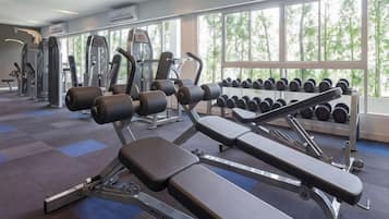 Une salle de sport équipée de machines d’exercice, d’haltères et dotée de grandes fenêtres.