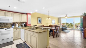 A kitchen with granite countertops, white cabinets, and a dining area with a table and chairs. - Walk 2 Beach~Spacious Balcony~100ft2Bch~Fab Lagoon Pool~Sterling Shores 307 (Destin)