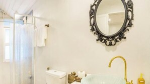 Et badeværelse med en vask i glas, en guldfarvet hane, et hvidt toilet, et hvidt håndklæde og et dekorativt spejl.