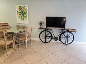 A dining area with a wooden table and chairs, a television on a stand, and a bicycle. - SB#4: Pet Friendly 1BR: Beach Across Street (Pensacola)