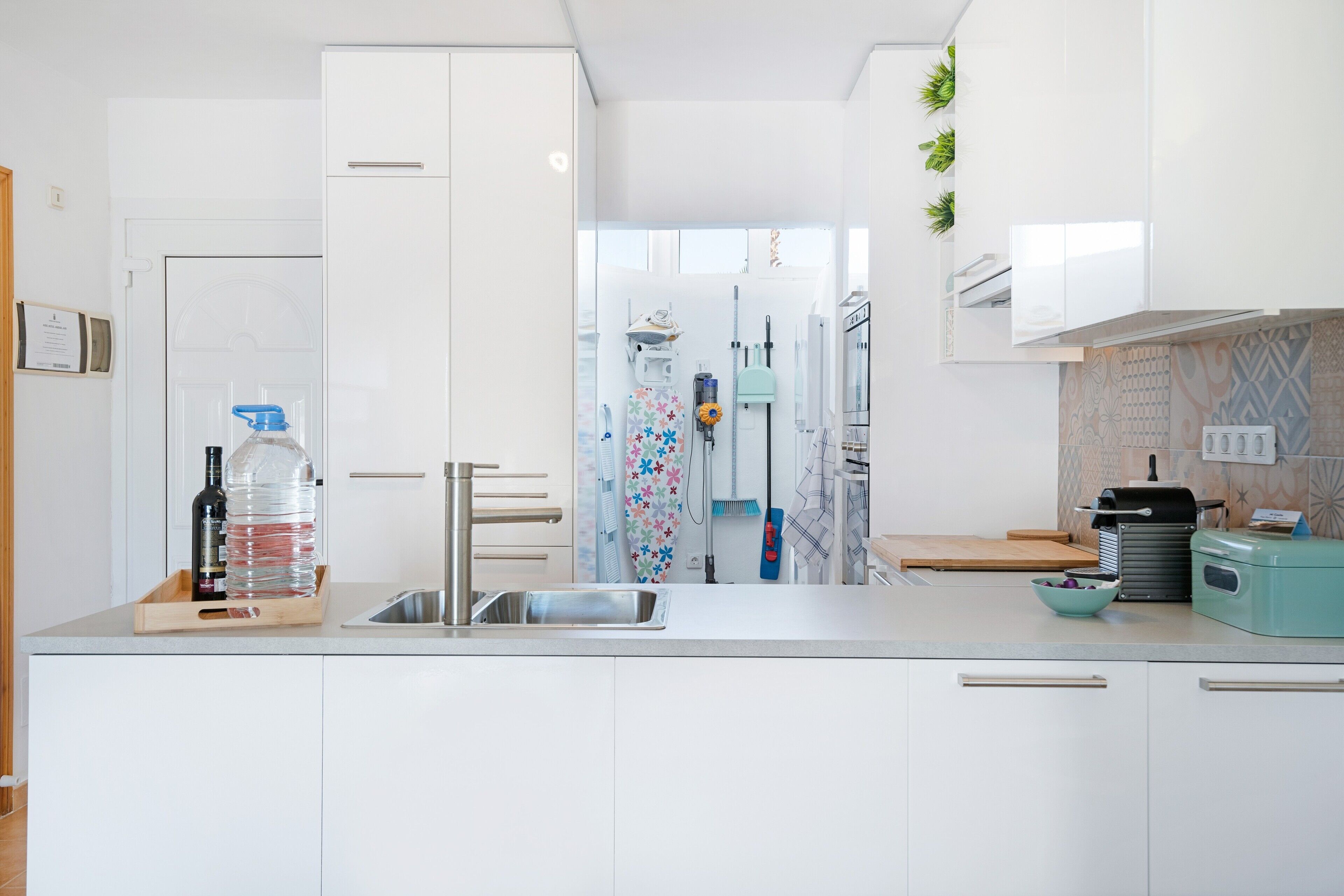 Une cuisine moderne avec des meubles blancs, un évier en acier inoxydable, un distributeur d’eau et un petit plan de travail sur lequel se trouve un saladier.