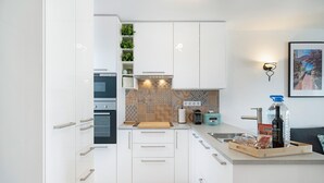Una cocina moderna con gabinetes blancos, horno empotrado, cafetera y tabla de cortar de madera.