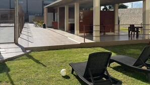 Een terras buiten met een overdekte zithoek, een gazon en een voetbal.