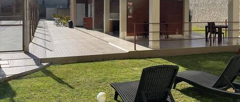An outdoor patio area with a covered seating area, a grassy lawn, and a soccer ball.