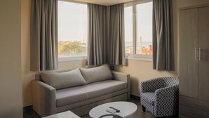 Een hotelkamer met een bank, een gestreept fauteuil, een tafeltje en een kledingkast.