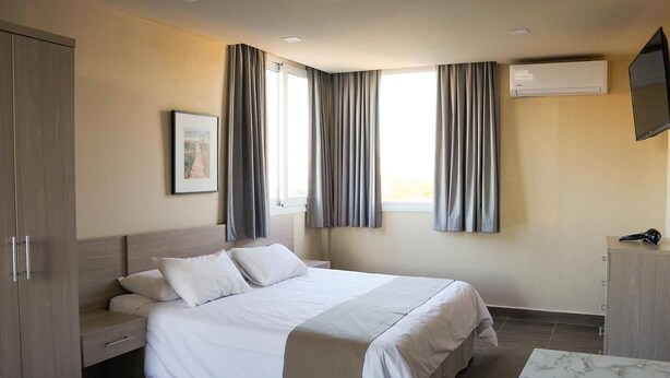 Een hotelkamer met een bed, een kledingkast, een bureau, een flatscreen televisie en een airconditioning.