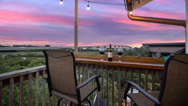 Een balkon met stoelen en een tafel, met uitzicht op een rivier en een brug bij zonsondergang.