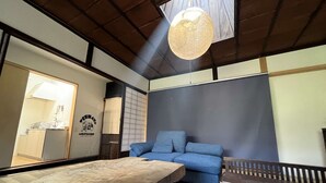 A room with a wooden table, blue sofa, and a hanging light fixture. - This inn is a renovated old house. (中津川市)