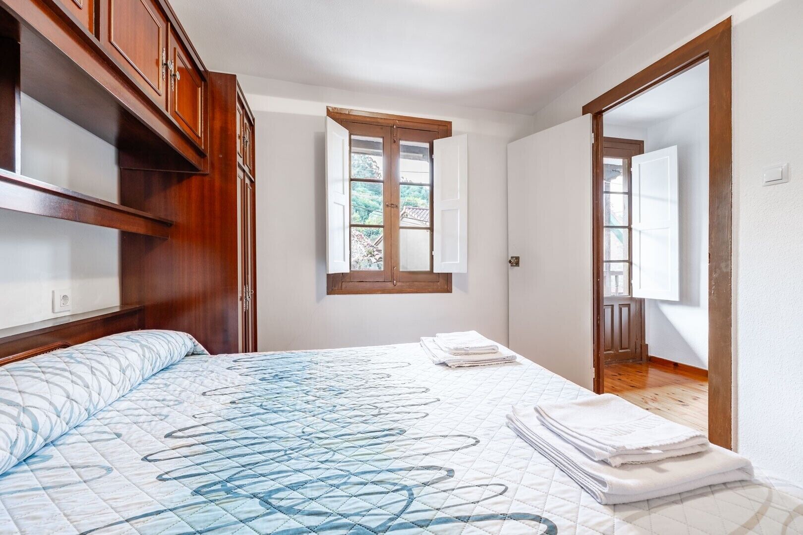 Un dormitorio con cama, ventana, puerta y armarios de madera.