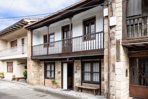 Un bâtiment à deux  étages avec des murs en pierre, un balcon doté d’une balustrade en bois et une porte avec une fenêtre.