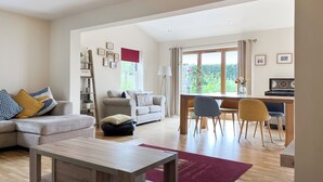 A spacious living room with a sofa, a coffee table, and a dining area with chairs and a piano.