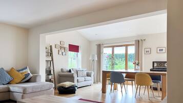A spacious living room with a sofa, a coffee table, and a dining area with chairs and a piano.