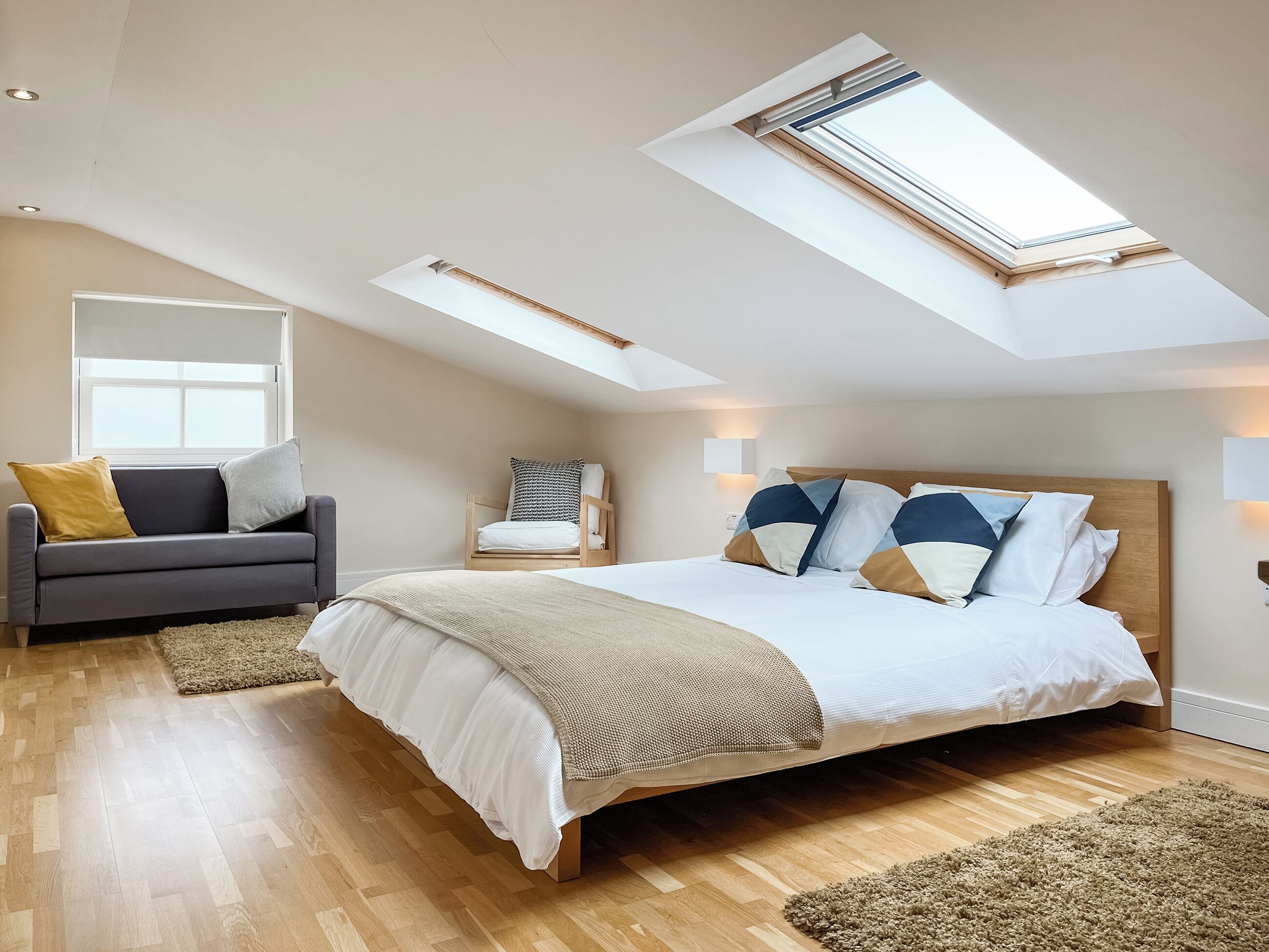 A bedroom with a large bed, a sofa, a chair, and a skylight.