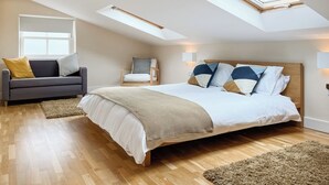 A bedroom with a large bed, a sofa, a chair, and a skylight.