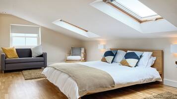 A bedroom with a large bed, a sofa, a chair, and a skylight.
