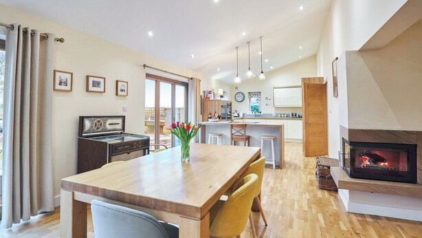 A modern kitchen with a central island, a dining area with a wooden table and chairs, and a fireplace.